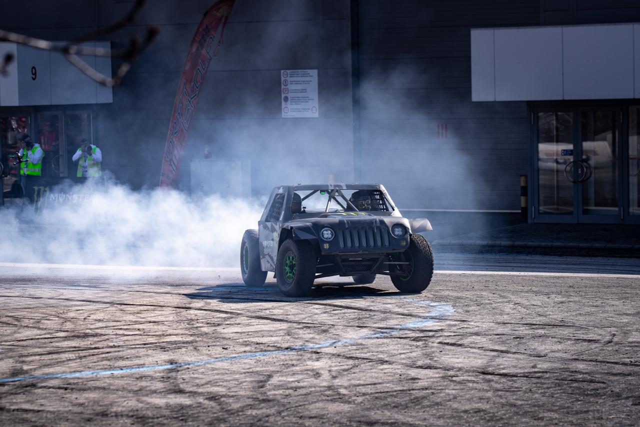 Monster Energy branded off-road buggy doing burnout at outdoor motorsport event