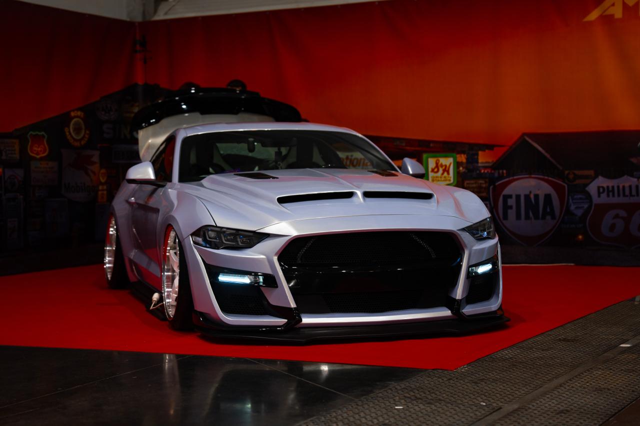 Custom white widebody Ford Mustang on red carpet at AMTS indoor auto show