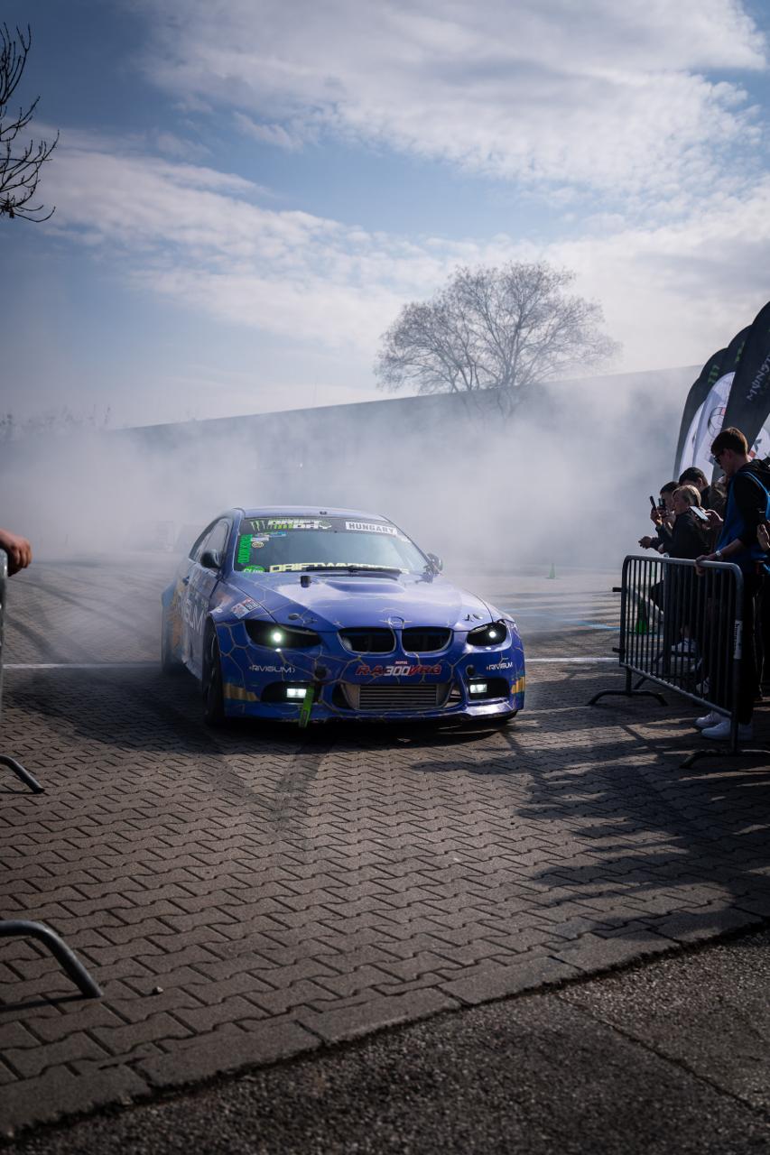 Blue BMW drift car sliding sideways through a cloud of tyre smoke at outdoor event