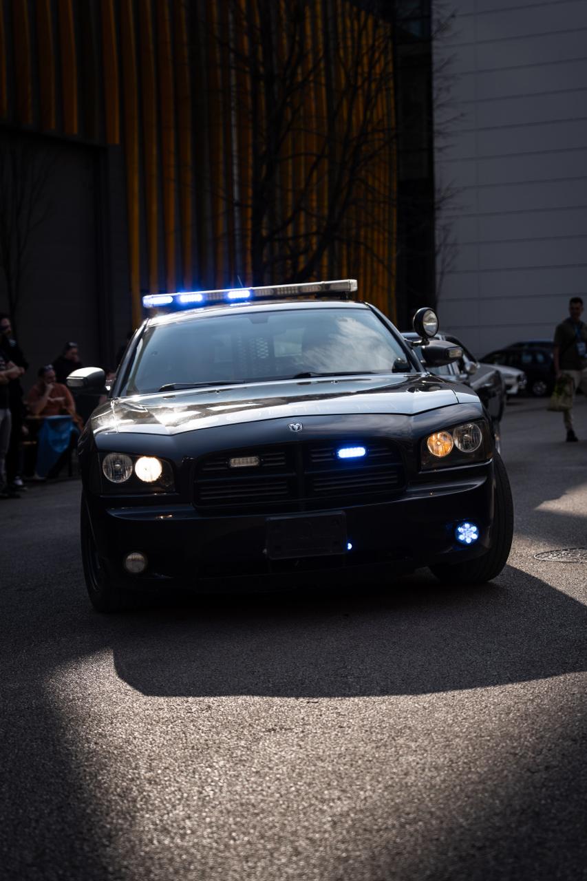 Black Dodge Charger police-style car with blue emergency lights at dusk