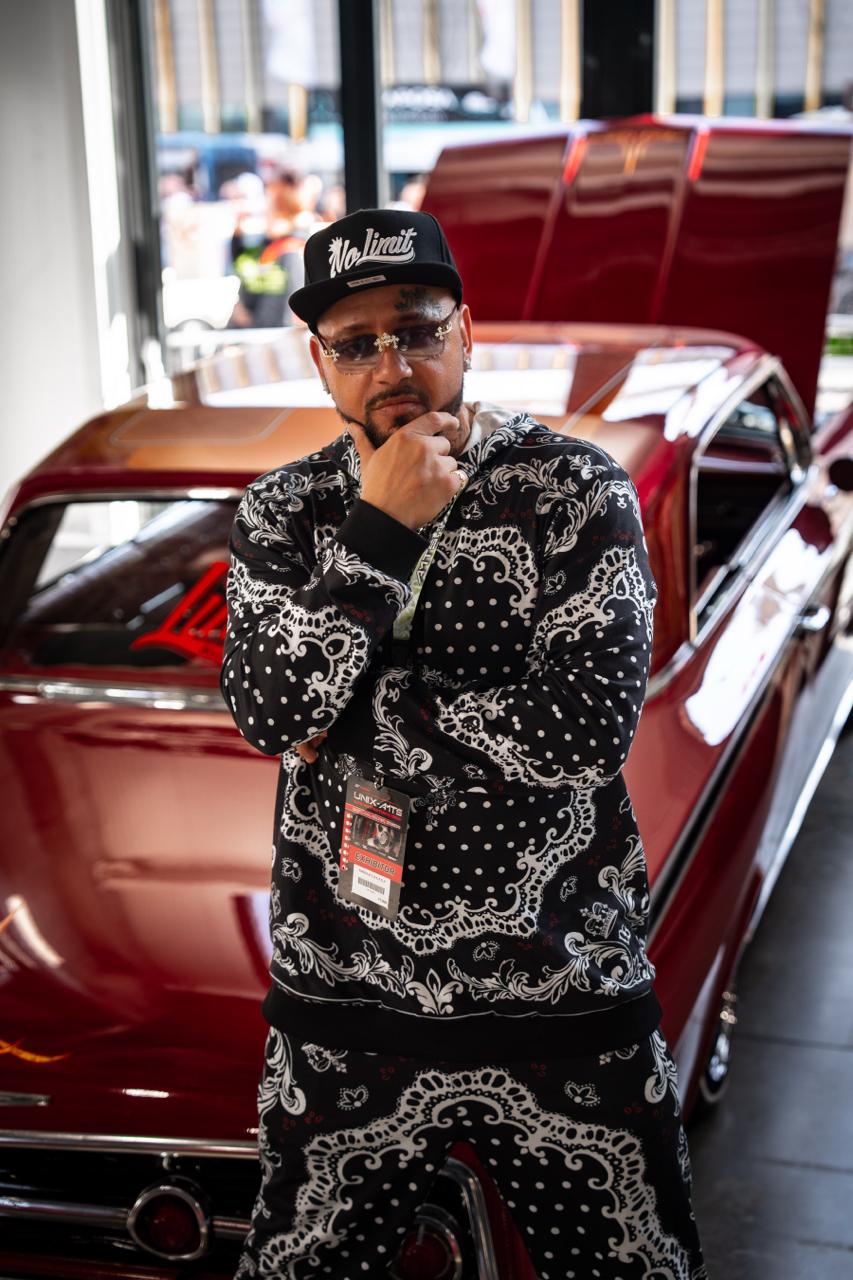 Portrait of man in paisley bandana outfit standing in front of cherry-red classic car at show
